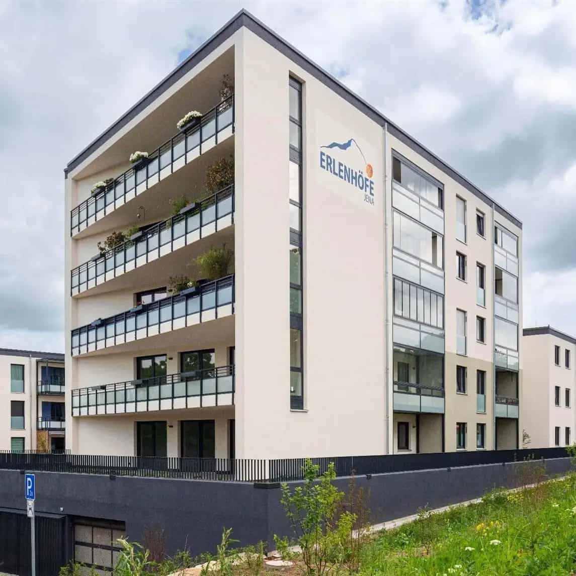 Mehrfamilienhaus mit Balkonen und bepflanzten Außenbereichen unter bewölktem Himmel.