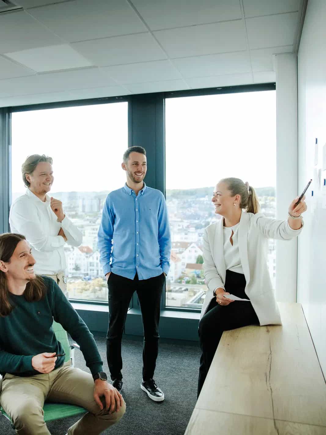 Fünf Personen in einem modernen Büro, die gemeinsam an einer Wand mit Notizzetteln Ideen besprechen.