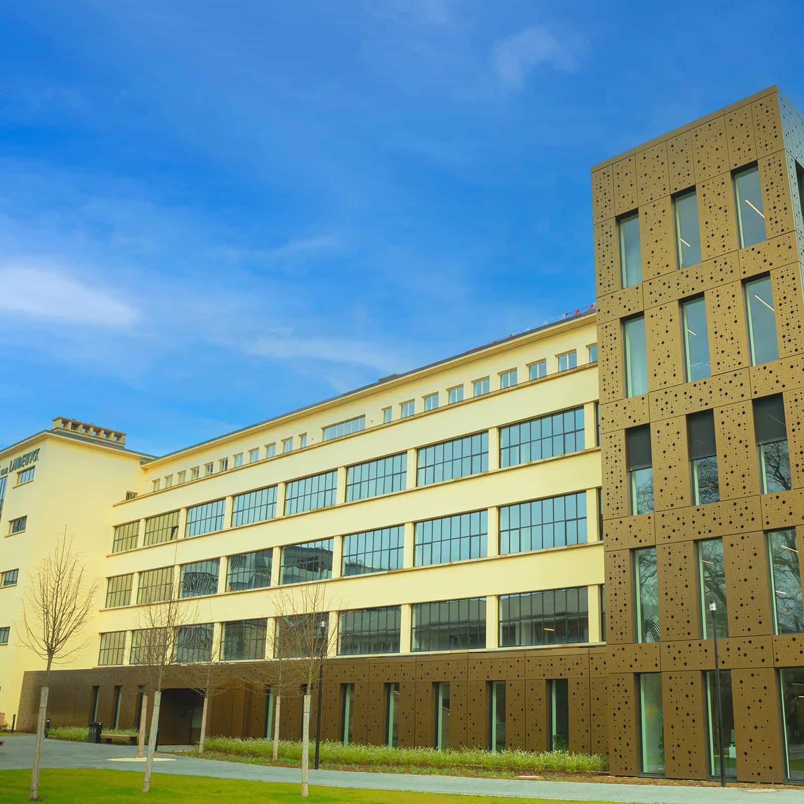 Modernes, mehrstöckiges Gebäude mit großen Fenstern und dekorativer Fassade vor blauem Himmel.