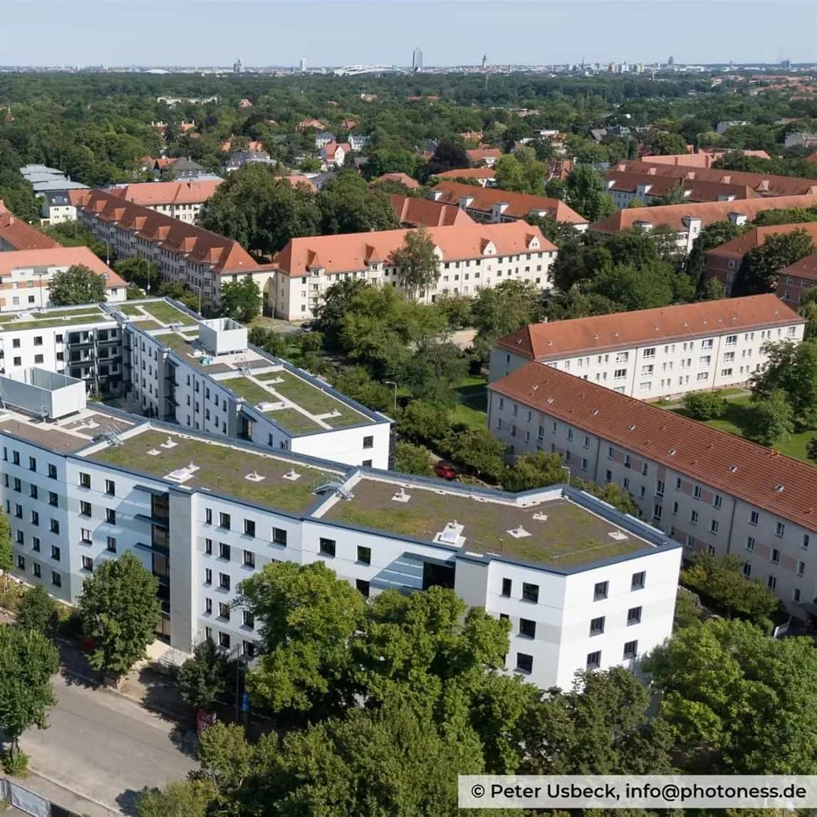 Moderne Wohnanlage mit begrünten Flachdächern in einer grünen Stadtumgebung, umgeben von Bäumen und traditionellen Gebäuden.