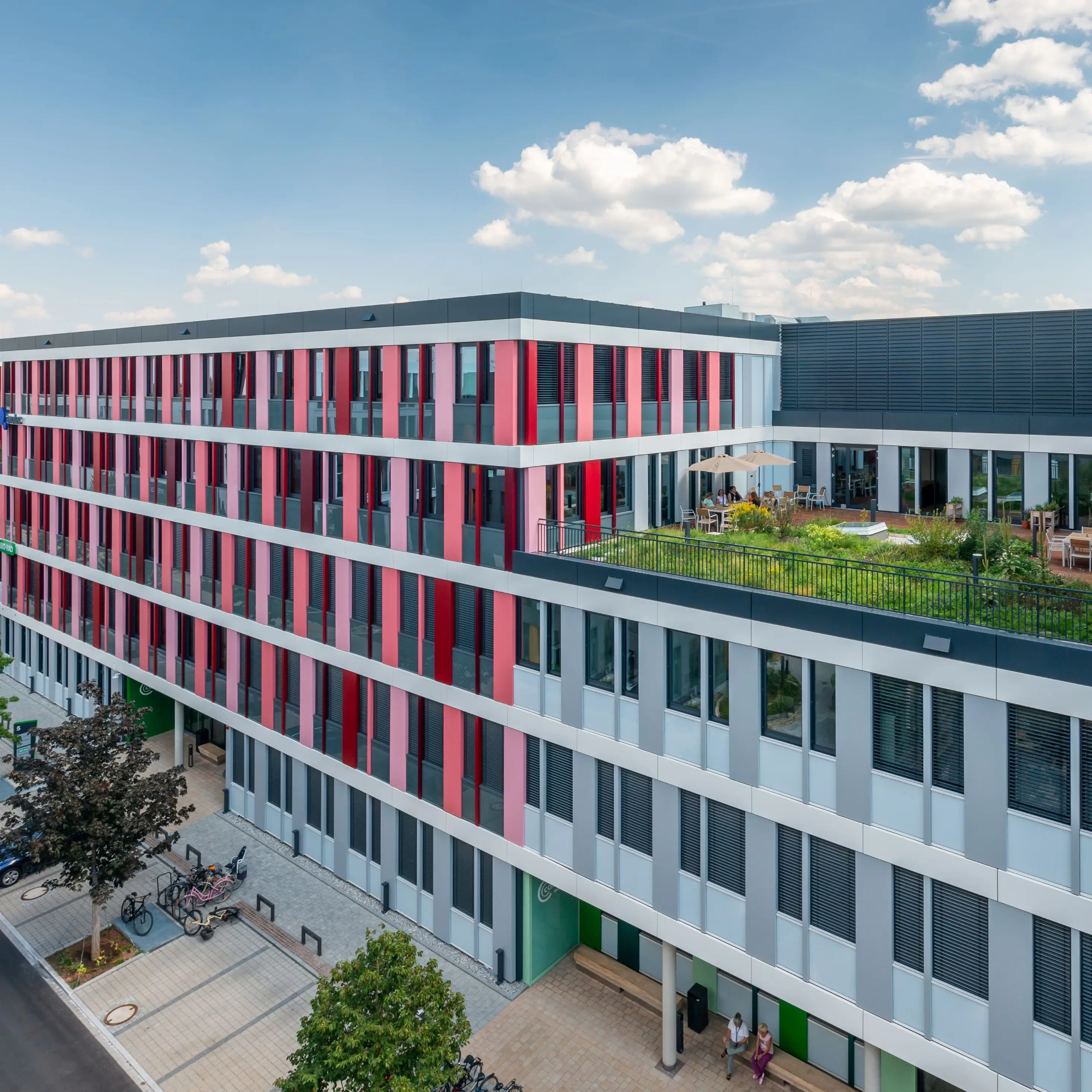 Modernes Bürogebäude mit farbiger Fassade und begrüntem Hof im urbanen Umfeld, bei sonnigem Wetter.